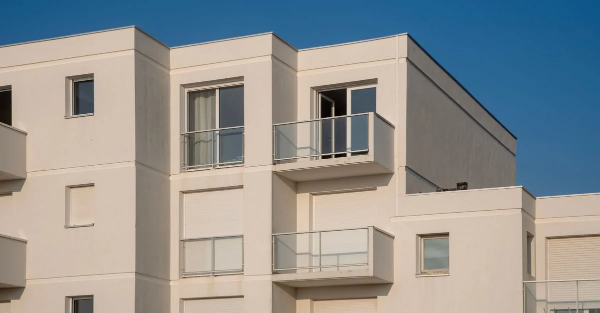 Vue d'un complexe d'appartements blancs contemporains sous un ciel bleu clair.