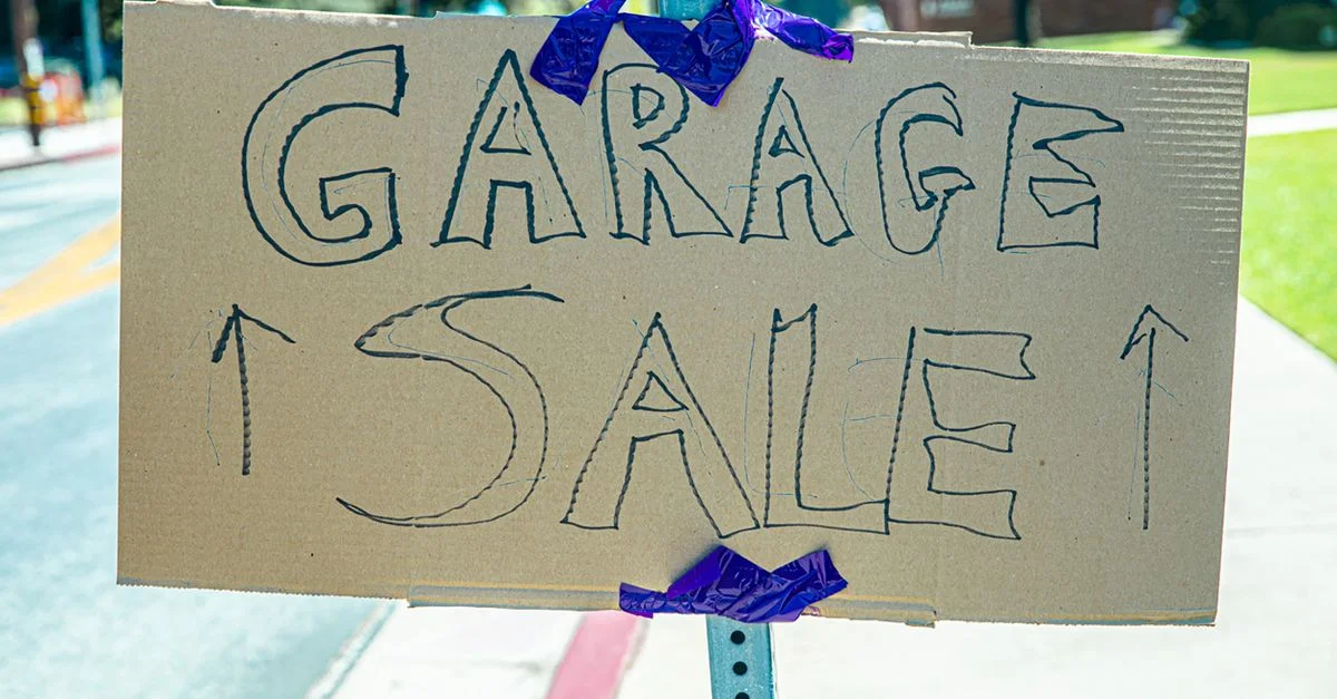 Un panneau de vente de garage écrit à la main, collé sur du carton, affiché en extérieur.