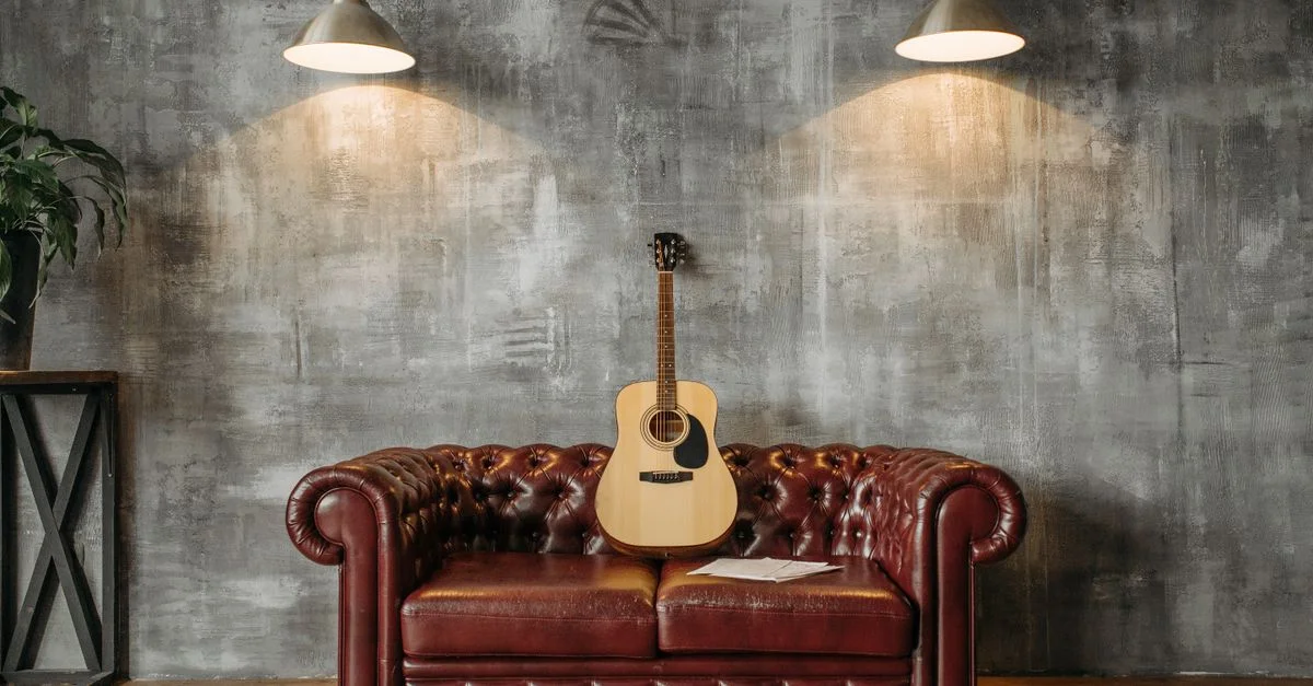 Un design d'intérieur élégant avec une guitare acoustique reposant sur un canapé en cuir rouge, éclairée par des suspensions.