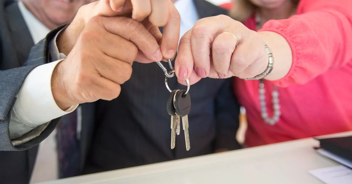 Des collègues d'affaires célébrant une transaction réussie avec une poignée de main et un échange de clés.