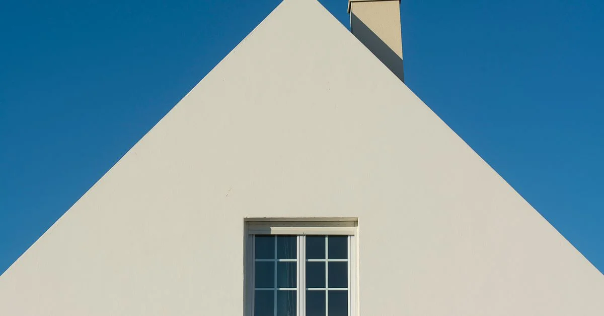 Façade de maison triangulaire simple avec fenêtre et cheminée contre un ciel bleu clair.