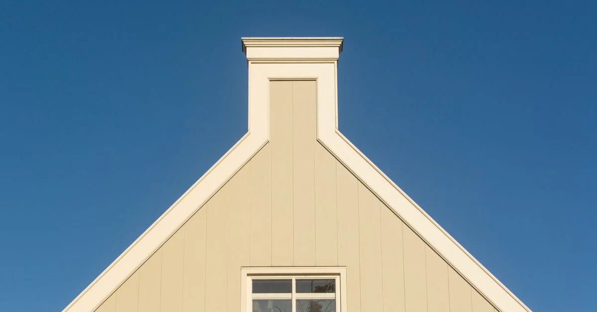 Façade de maison triangulaire contre un ciel bleu clair, présentant une architecture minimaliste.
