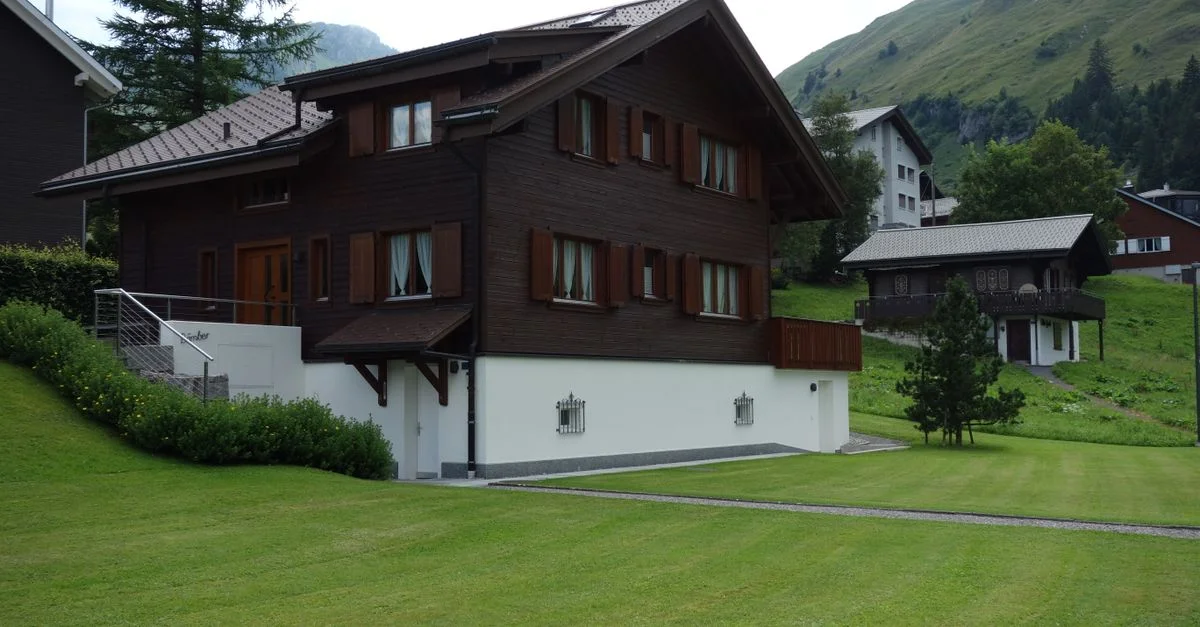 Une maison en bois pittoresque dans les Alpes, entourée de verdure luxuriante, parfaite pour des thèmes de voyage ou d'architecture.