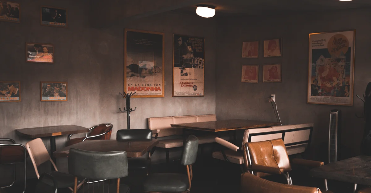Intérieur de café rétro avec décor vintage et affiches sur murs en béton, éclairage chaleureux.