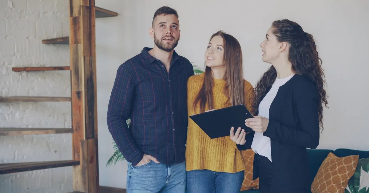 Jeune couple explorant une nouvelle maison avec leur agent immobilier, discutant des options et des caractéristiques.