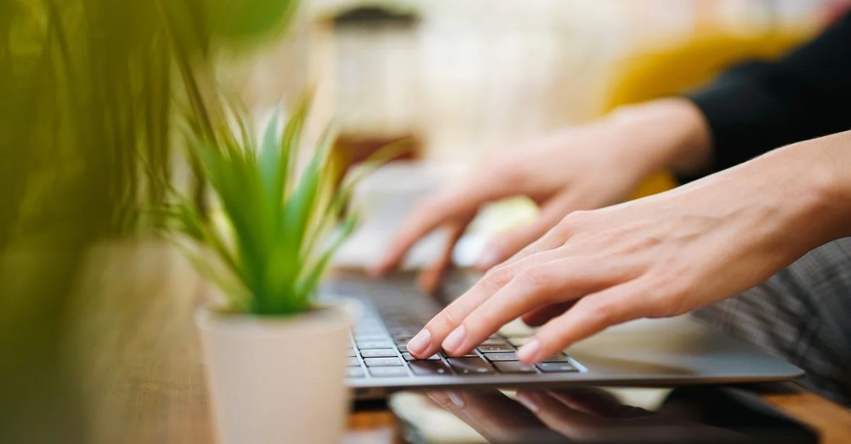 Des mains qui tapent sur un ordinateur portable dans un cadre intérieur avec une plante verte. Parfait pour les concepts de travail à domicile.