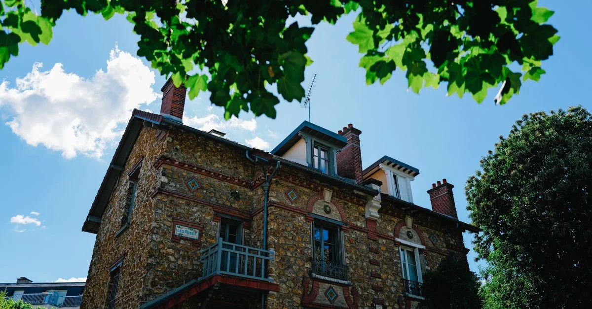 Charmante maison historique en pierre avec une végétation estivale luxuriante sous un ciel bleu éclatant.