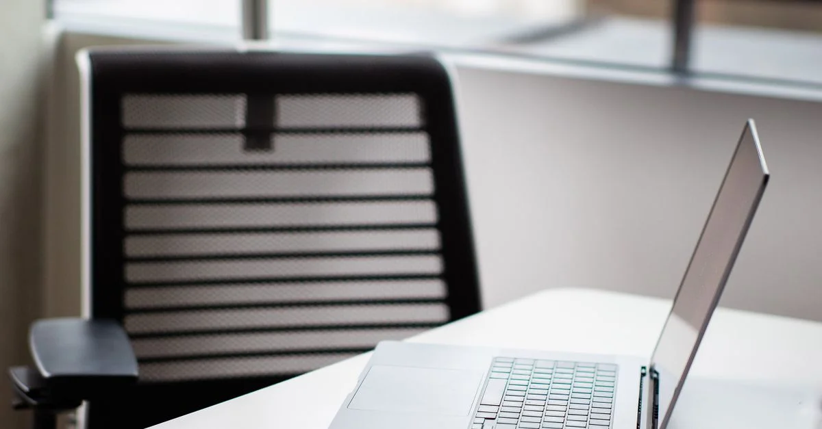 Un ordinateur portable élégant sur un bureau blanc dans un cadre de bureau contemporain avec une chaise en maille.