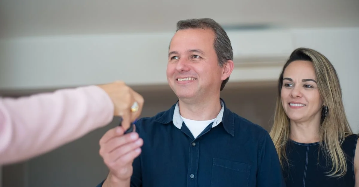 Couple souriant recevant des clés, célébrant l'achat de leur nouvelle maison à l'intérieur.