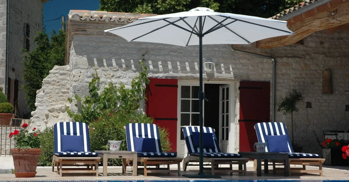 Détendez-vous près de la piscine de la maison en pierre avec des transats et des parasols dans une cour ensoleillée.