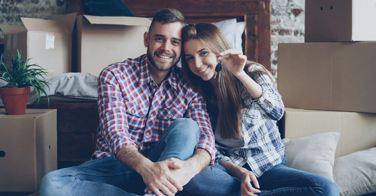 Couple souriant tenant des clés au milieu des cartons de déménagement dans leur nouveau foyer.