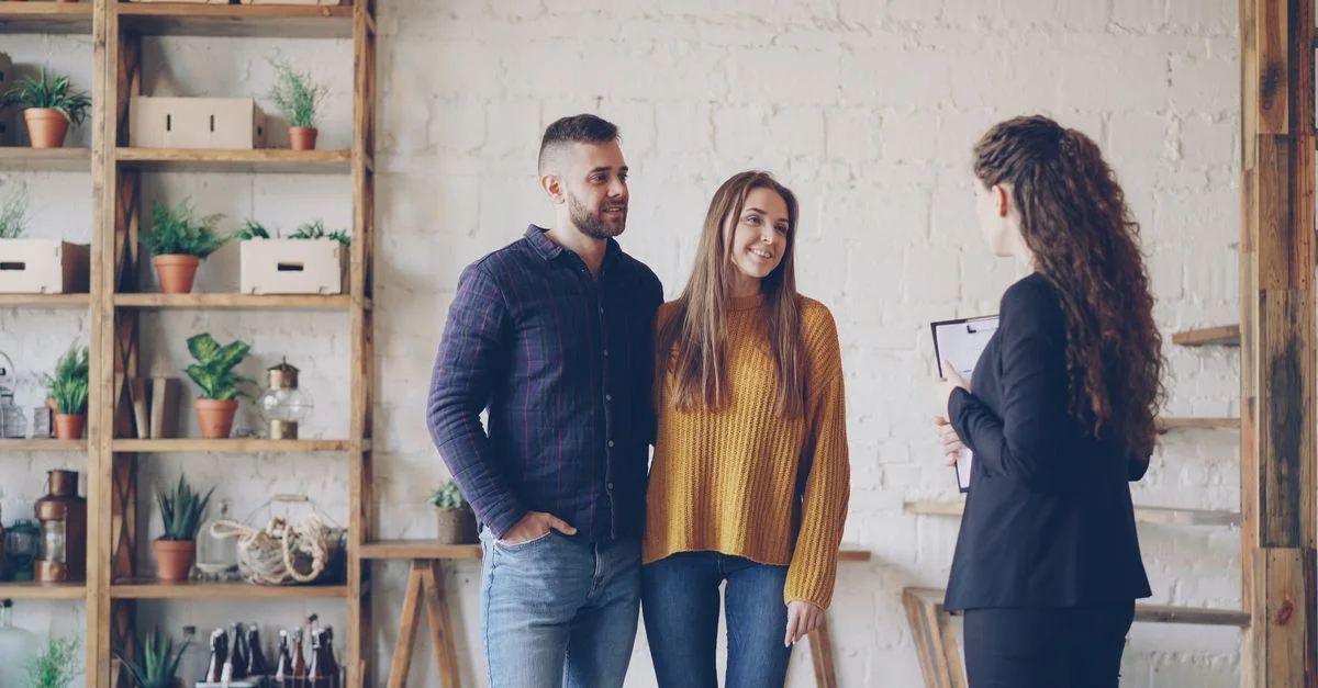 Jeune couple discutant avec un agent immobilier dans un cadre intérieur moderne.