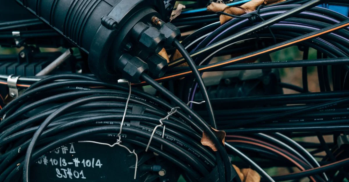 Vue en gros plan de câbles noirs entrelacés et de connecteurs dans une installation télécom extérieure.