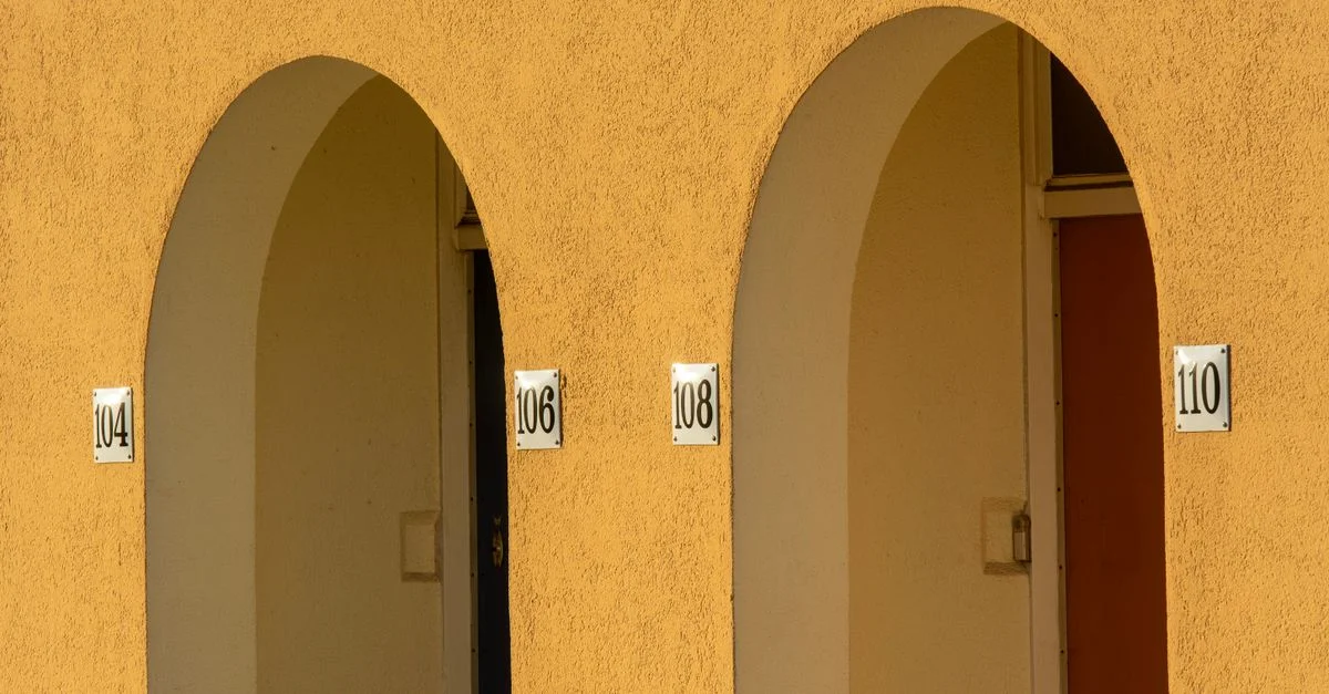 Gros plan sur des murs jaunes en arc avec des numéros d'appartement dans un cadre urbain.