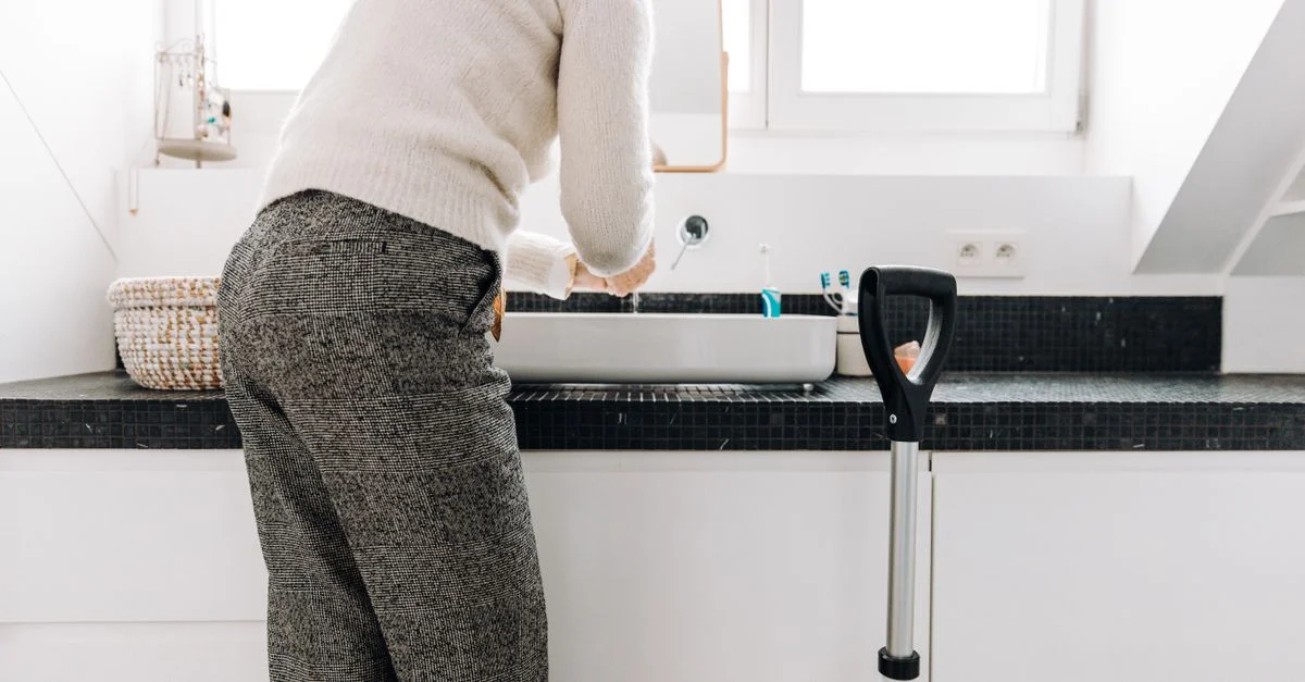 Une personne âgée se lave les mains dans une salle de bain moderne, mettant en avant l'hygiène et l'indépendance.