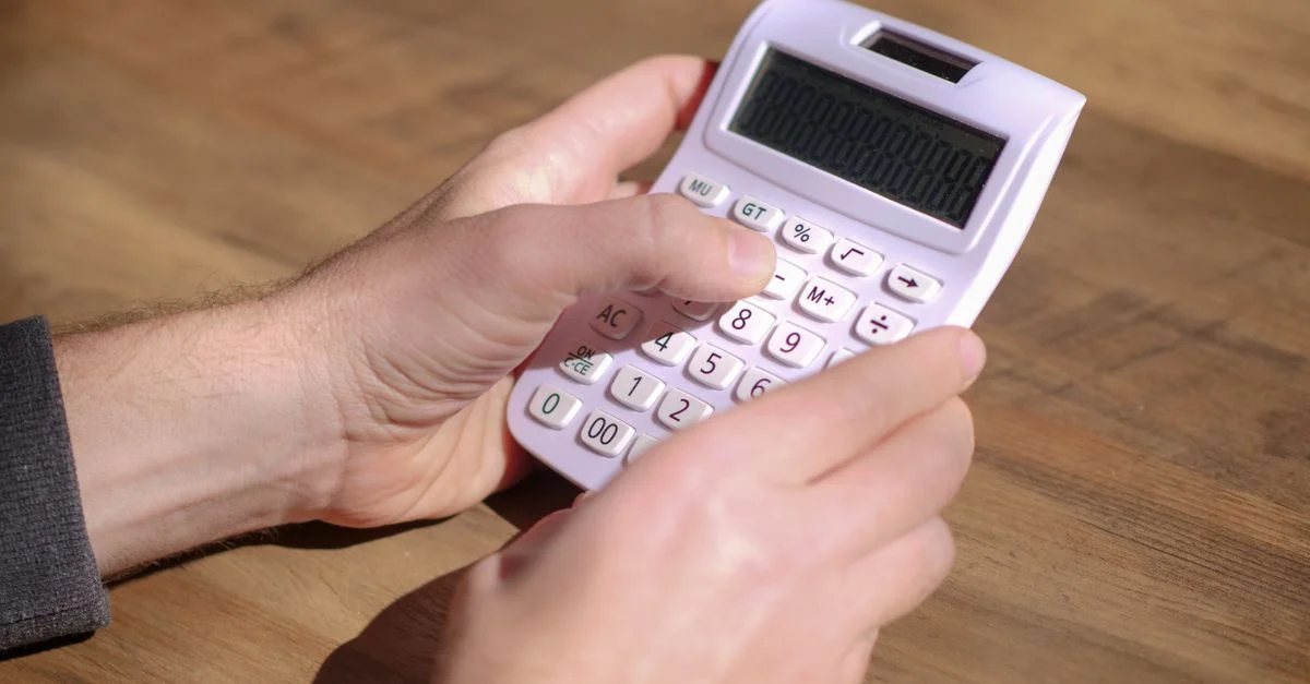 Mains utilisant une calculatrice rose sur une table en bois, mettant l'accent sur le calcul et les mathématiques.