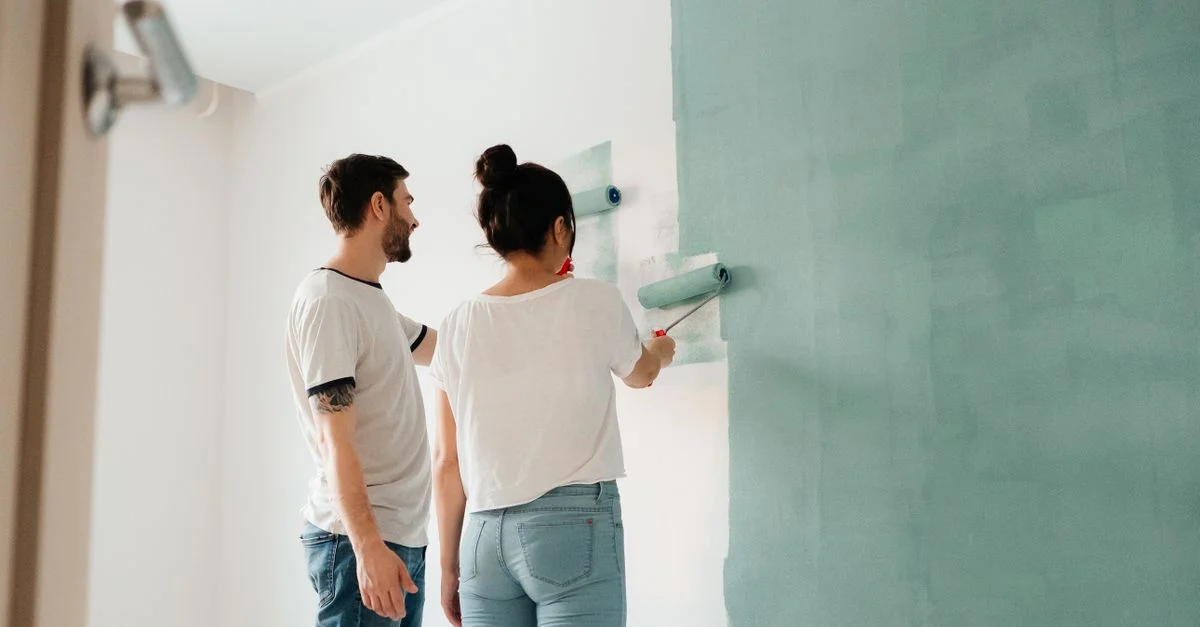 Un couple collabore pour peindre un mur avec un rouleau à l'intérieur, illustrant l'esprit d'équipe.